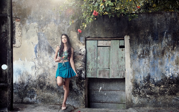 Woman leaning against a weathered wall with a wooden door