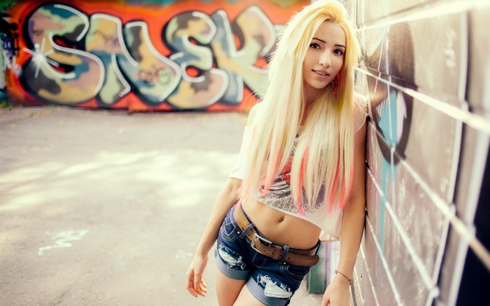 Young woman with blonde hair and pink streaks leaning against graffiti wall