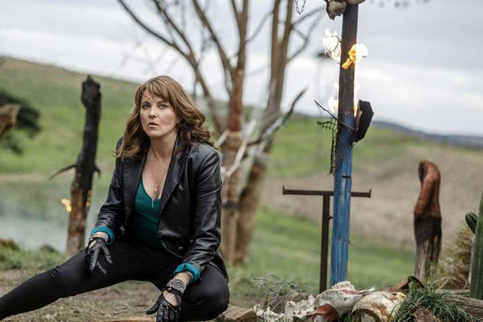 Lucy Lawless crouching outdoors