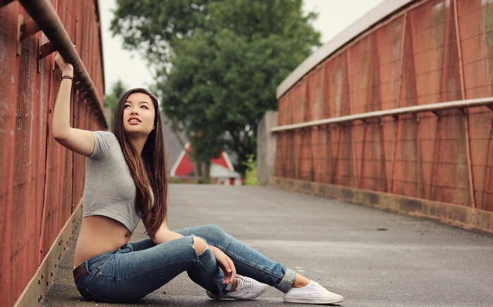 Woman in ripped jeans and crop top sitting on a bridge