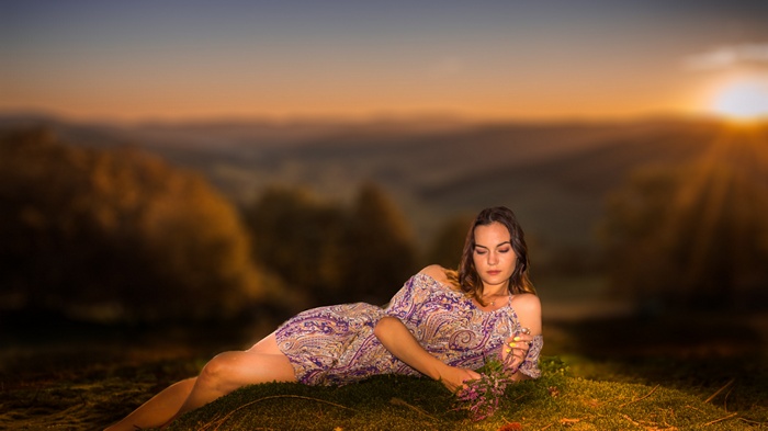 Woman in dress lying in grass at sunset