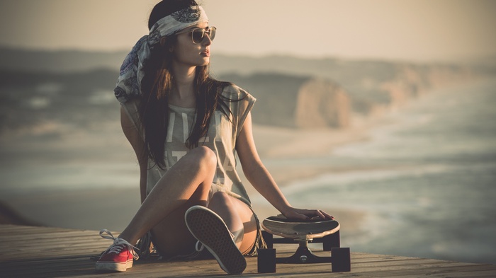 Woman with bandana and sunglasses sitting with skateboard