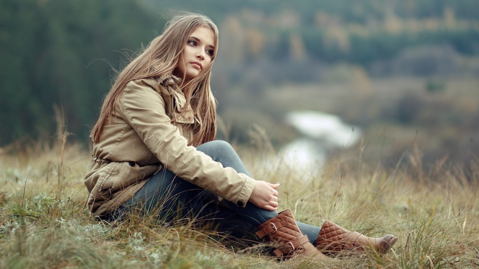 Young woman sitting on a grassy hill overlooking a river