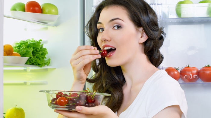 Woman eating cherries from a bowl in a refrigerator