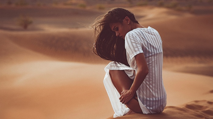 Woman in white dress crouching in desert dunes