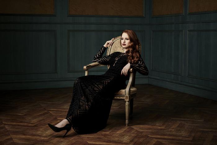 Madelaine Petsch in a black dress sitting on a chair