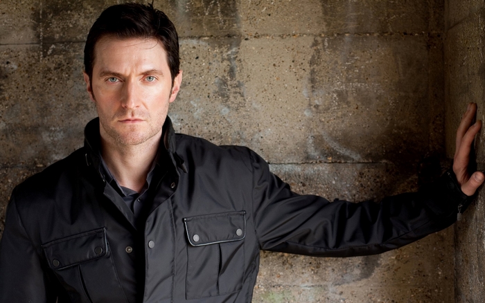 Richard Armitage leaning against a concrete wall