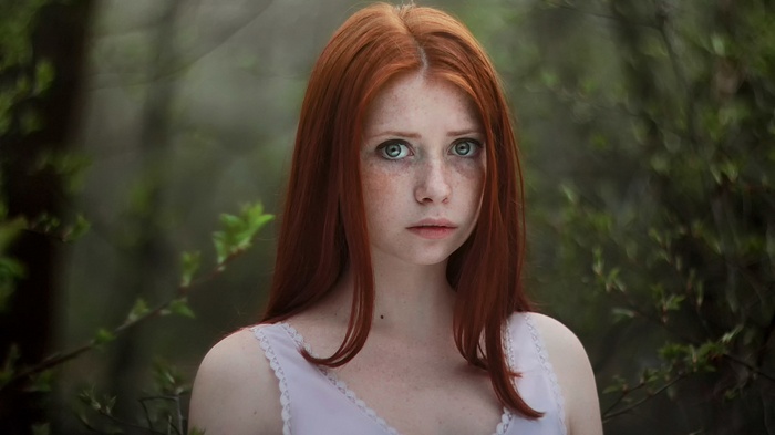 Young woman with red hair and freckles in a forest