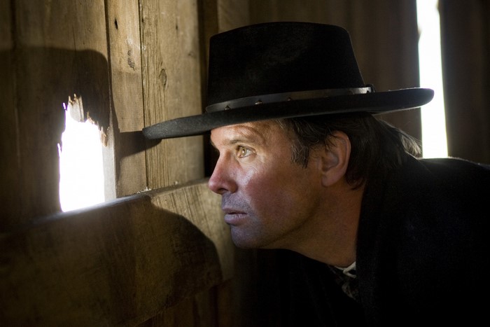 Walton Goggins peeking through a hole in a wooden wall