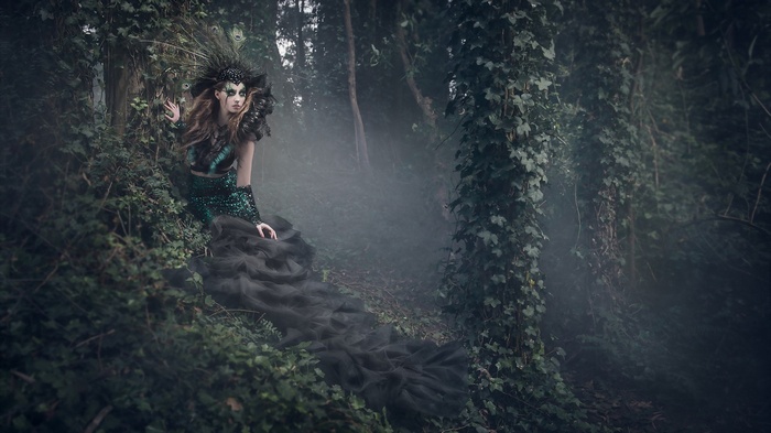 Woman in peacock-themed costume in a misty forest