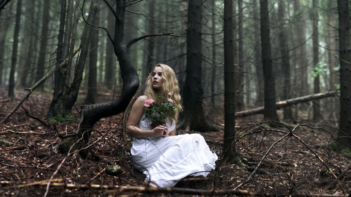 Woman in white dress holding flowers in a dark forest