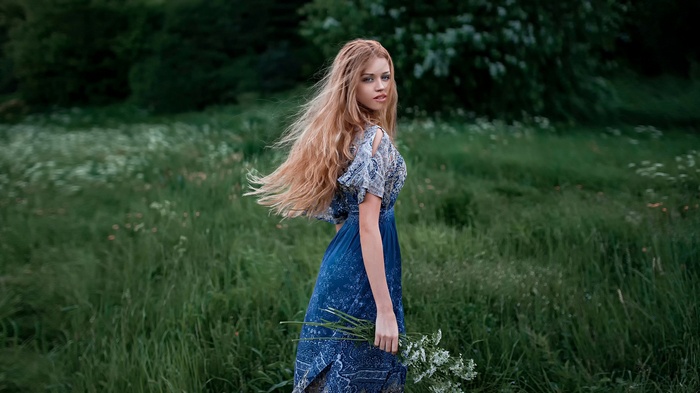 Woman in a blue dress holding flowers in a field