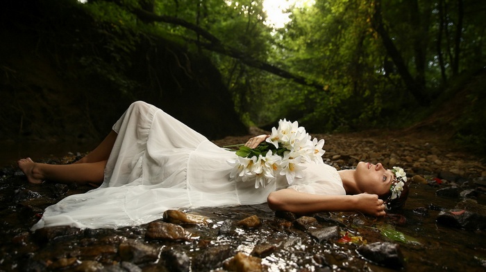 Woman in white dress lying in a stream with flowers