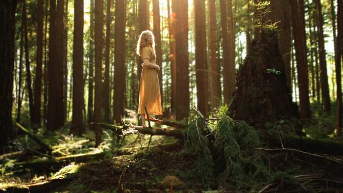 Woman in yellow dress standing in a sunlit forest