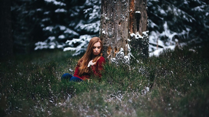 Woman in red sweater sitting by a tree in winter forest