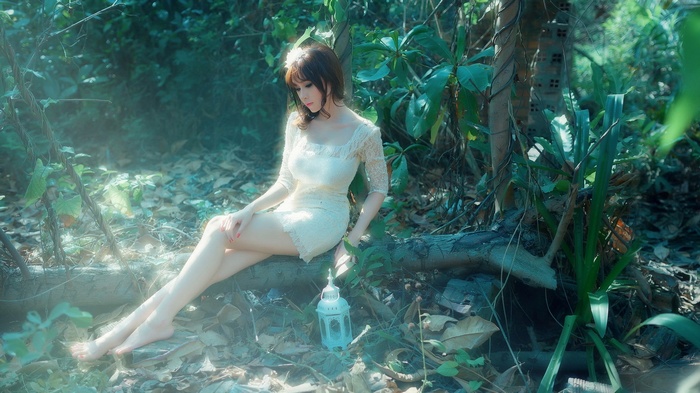 Woman in white dress sitting in a forest with a lantern