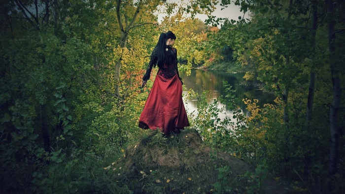 Woman in red dress standing by a river in a forest