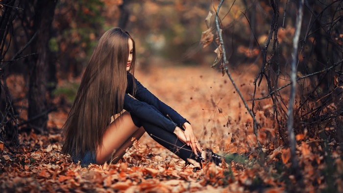 Woman with long hair sitting in autumn leaves