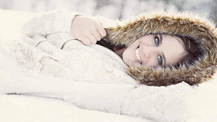 Woman in a fur-lined hooded jacket lying in snow