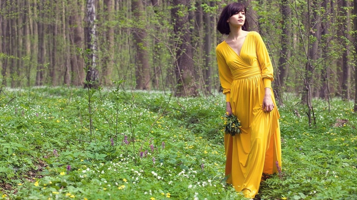 Woman in yellow dress holding flowers in a forest
