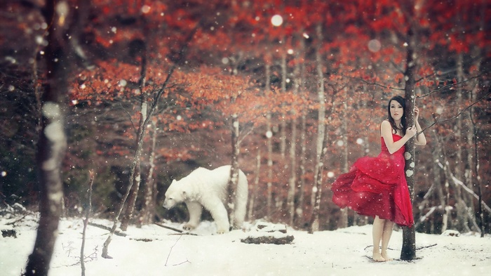 Woman in red dress with polar bear in snowy forest