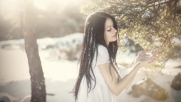 Woman in white dress holding snow in a winter forest
