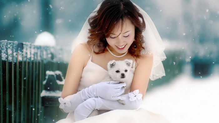 Bride holding a white dog in the snow