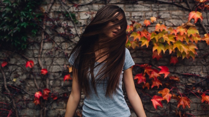Woman with long brown hair in front of a brick wall with ivy