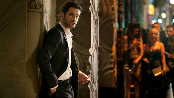 Tom Ellis in a suit leaning against a building at night
