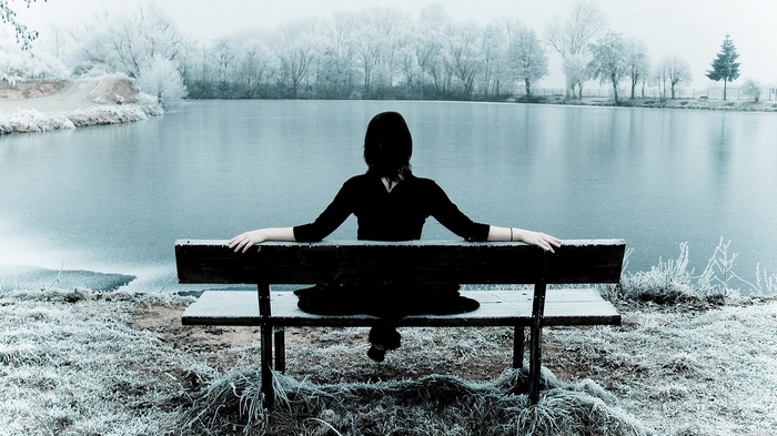 Woman in black sitting on a bench by a frozen lake