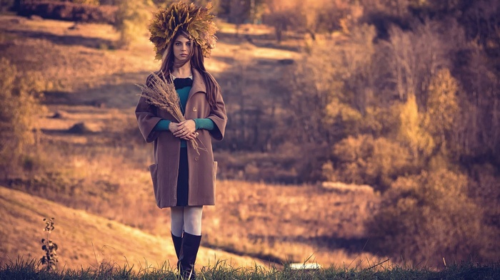 Woman with leaf crown holding wheat in autumn landscape