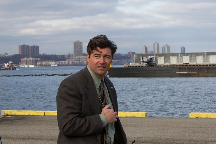 Kyle Chandler on a pier with a helicopter and city in background