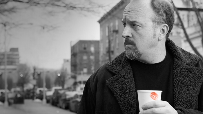 Louis C.K. holding a coffee cup in a city
