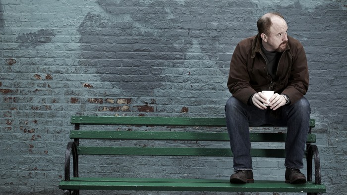 Louis C.K. sitting on a bench