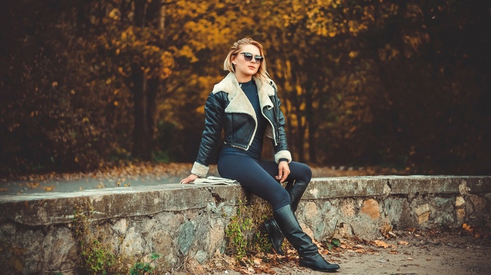 Woman in leather jacket sitting on a stone wall
