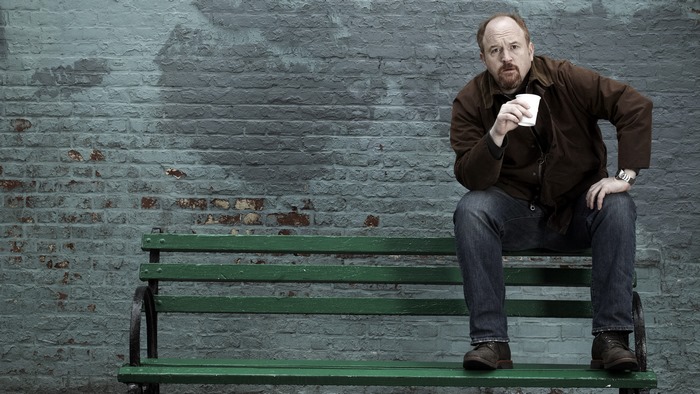Louis C.K. sitting on a bench with coffee