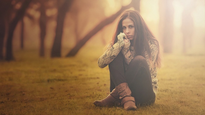 A young woman sits alone in a foggy forest