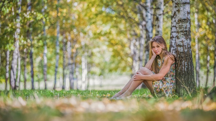 Girl sitting by a birch tree in a forest