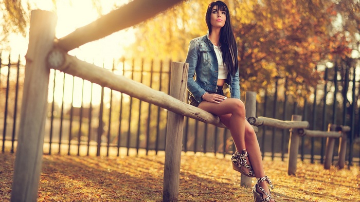 Woman sitting on a wooden fence in autumn