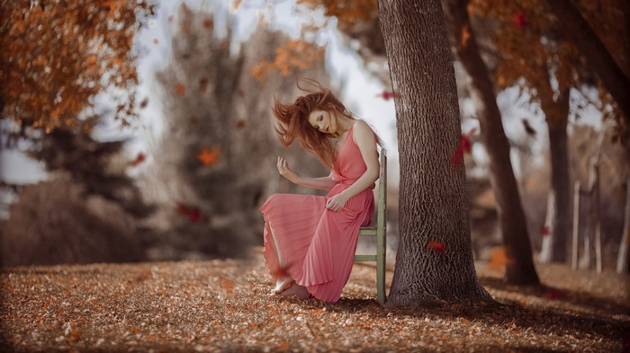 Woman in pink dress sitting by a tree in autumn