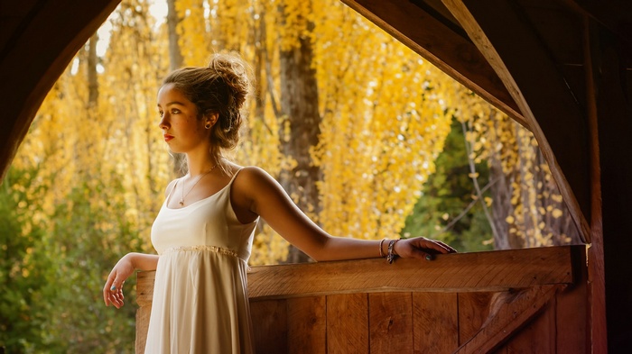 Young woman in white dress looking out from wooden structure