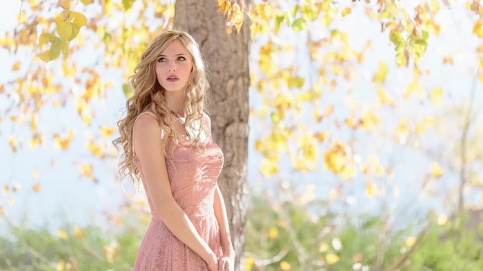 Young woman in pink dress standing near a tree