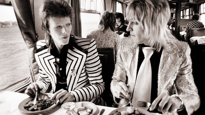 David Bowie and Mick Ronson eating on a train