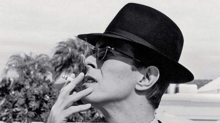 David Bowie wearing a hat and sunglasses smoking