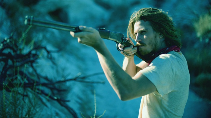 Garrett Hedlund aiming a rifle in a desert