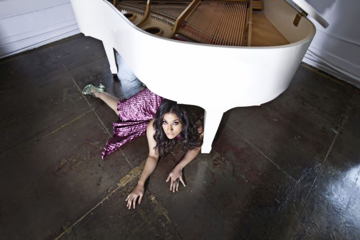 Janina Gavankar lying under a white grand piano