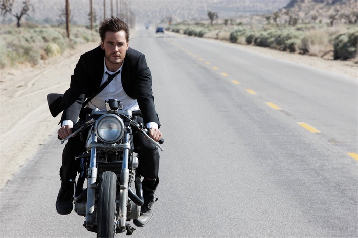 Taylor Kitsch riding a motorcycle on a desert road