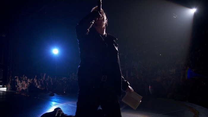 Bono performing on stage with a spotlight