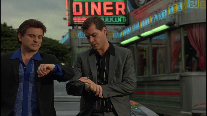 Two men checking watches in front of a diner
