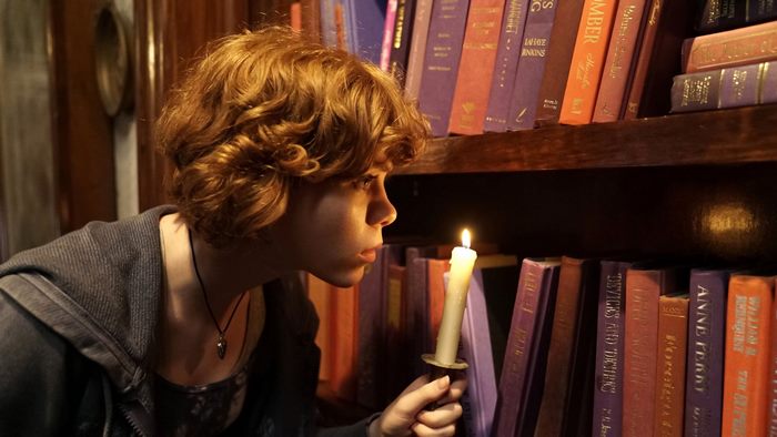 Sophia Lillis holding a candle in a library